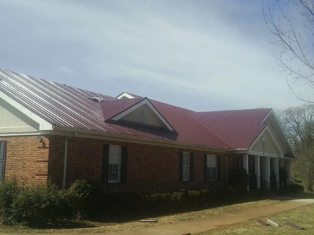Red metal roof with gabled entries on a long brick building, from a Hail Damage Roof Repair job in Poway