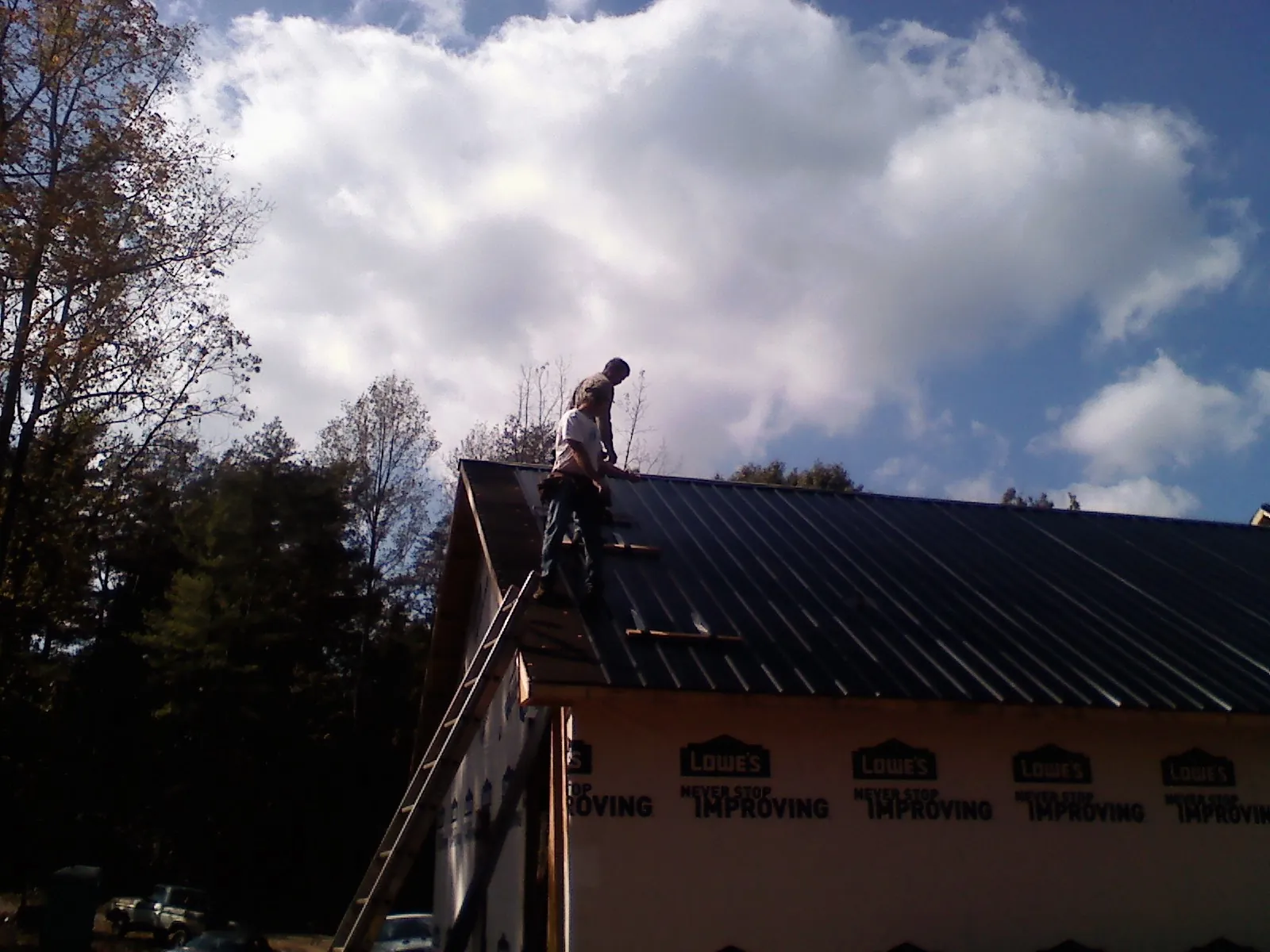 Roofer fastening dark metal panels high against a cloudy sky, from a Roof Inspection job in Poway