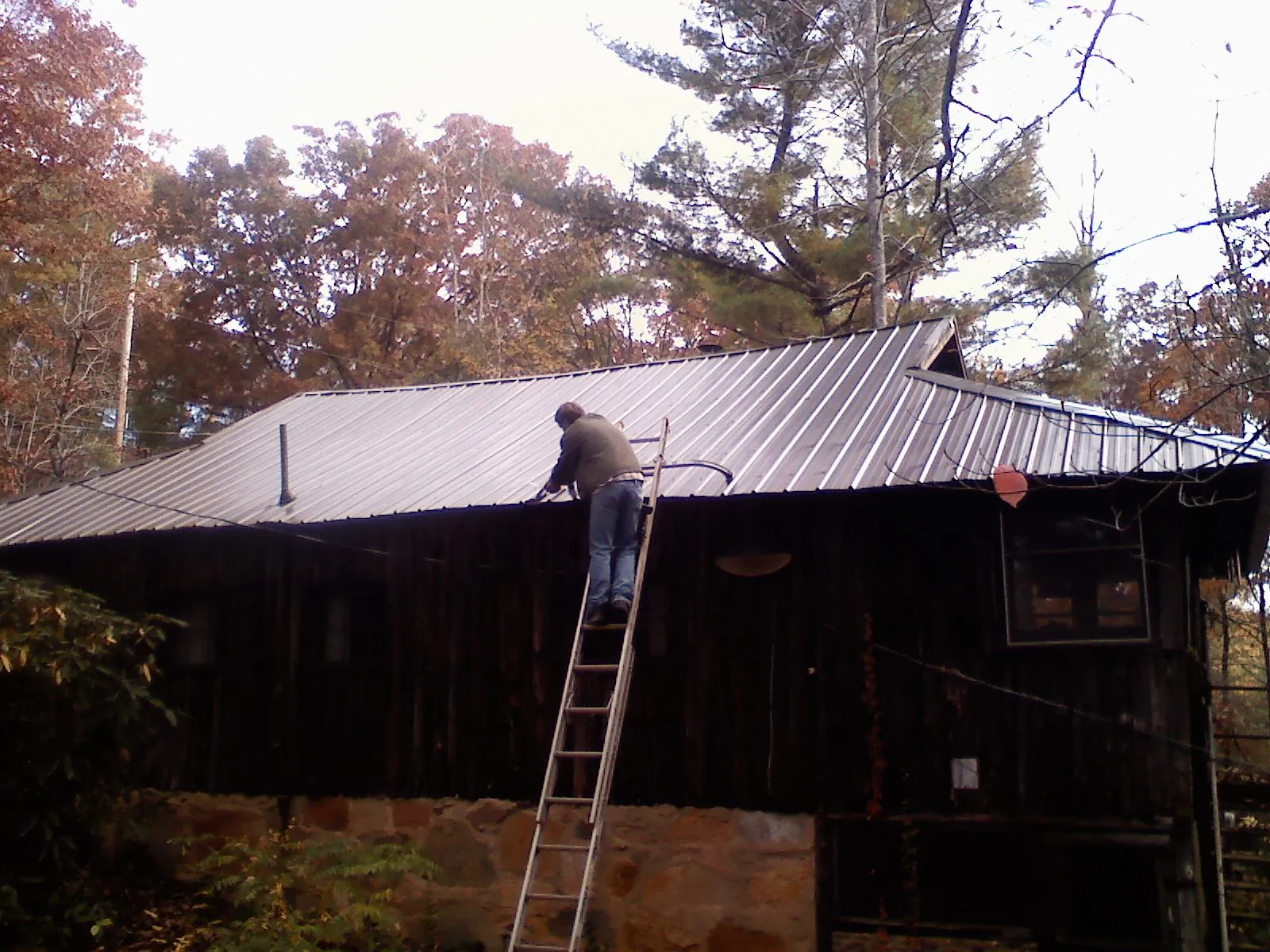 Roofer on a ladder working along the edge of a cabin metal roof in Poway